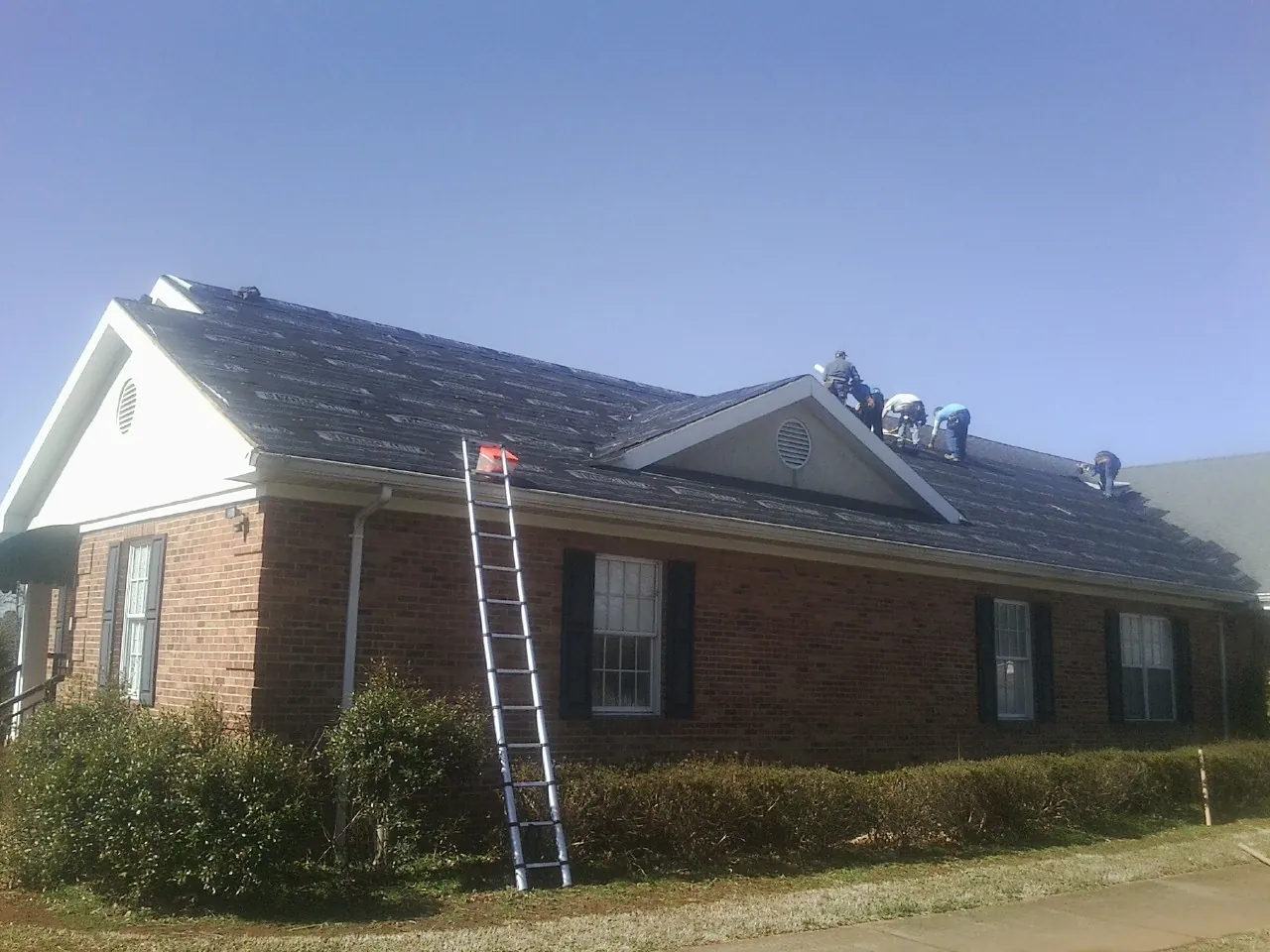 Crew tearing shingles off a brick ranch roof with a ladder set — Emergency Roof Repair work by our crew in Brookdale