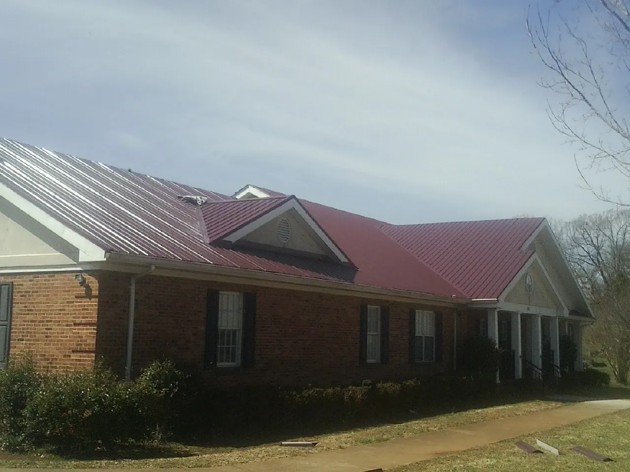 Red metal roof with gabled entries on a long brick building, from a Hail Damage Roof Repair job in Brookdale