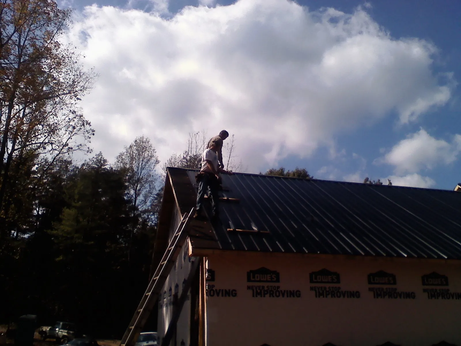 Roofer fastening dark metal panels high against a cloudy sky, from a Roof Inspection job in Brookdale